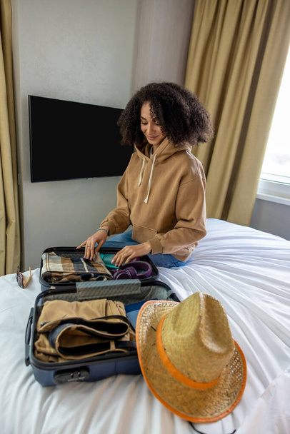 Ready for vacation. Curly-haired pretty young woman packing her suitcase - Φωτογραφία, εικόνα