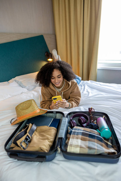Ready for vacation. Curly-haired pretty young woman packing her suitcase - Fotoğraf, Görsel