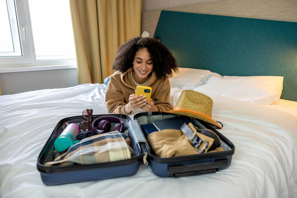 Ready for vacation. Curly-haired pretty young woman packing her suitcase - Foto, Imagem