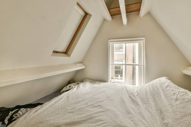 a bed in the corner of a room with an open window on one side and a white blanket on the other - Foto, Bild