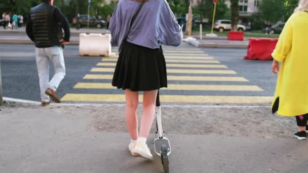 Vista posterior de la joven con scooter de pie esperando la luz verde en el paso de peatones. Gente montando scooter eléctrico en la calle de la ciudad. - Imágenes, Vídeo
