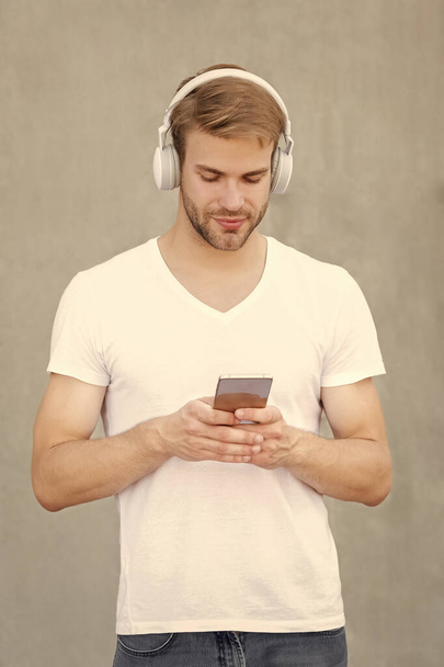 young man choose mp3 music playlist wearing white shirt. photo of man mp3 music playlist in headphones. man open mp3 music playlist. man use mp3 music playlist outside. - Fotoğraf, Görsel
