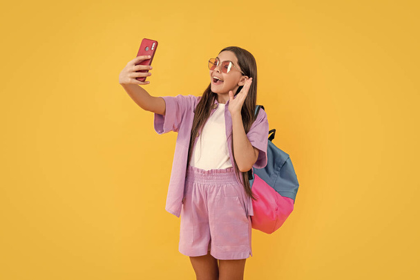 amazed teen selfie school girl on background. photo of teen selfie school girl with phone. teen selfie school girl isolated on yellow. teen selfie school girl in studio. - Fotoğraf, Görsel