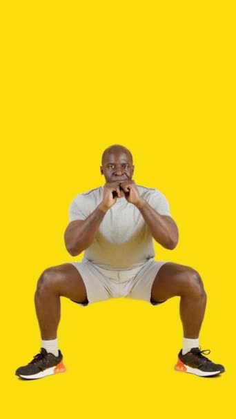 Video in studio met gele achtergrond van een sterke Afrikaanse man die sumo squats doet - Video