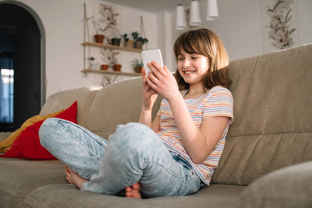 Genç bir kız evdeki kanepede oturur ve cep telefonu kullanır, sohbet eder ve arkadaşlarını arar. Gençler ve teknoloji.  - Fotoğraf, Görsel