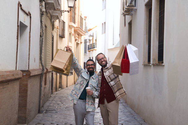 Real marriage of gay couple, walking down the street, hands full of shopping bags, happy and funny. Concept lgtb, lgtbiq+, couples, in love, shopping, sales. - Фото, изображение