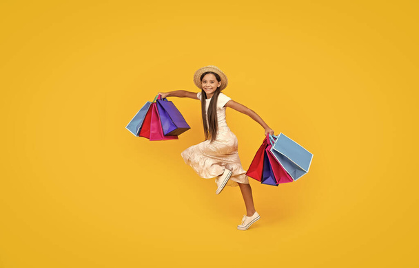 happy teen girl hurry with shopping bags on yellow background. full length. - Foto, Imagem