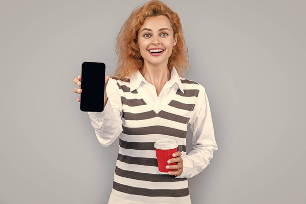 happy woman presenting application in studio. woman presenting application with phone. photo woman presenting application. woman presenting application isolated on grey background. - 写真・画像