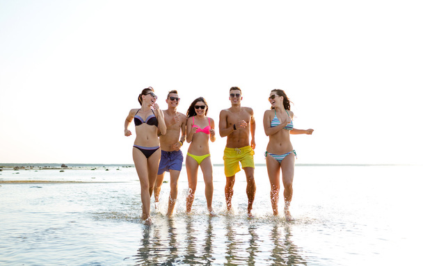 улыбающиеся друзья в солнечных очках, бегущие по пляжу
 - Фото, изображение