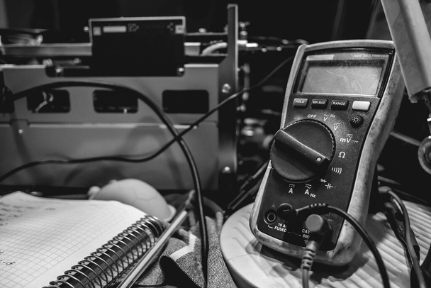 Electronics expertise: multimeter, open electronic equipment and a notebook on a table (in black and white) - Fotografie, Obrázek