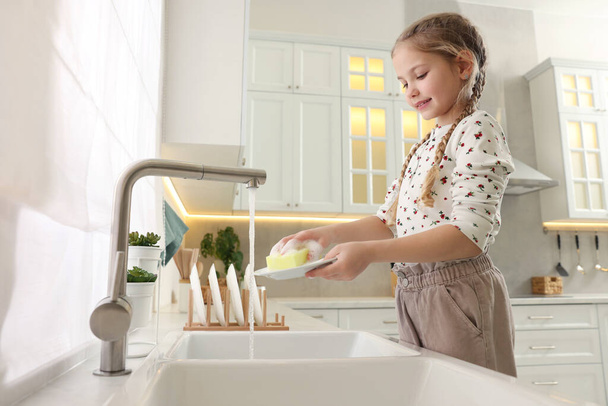 Little girl washing plate above sink in kitchen - Фото, зображення