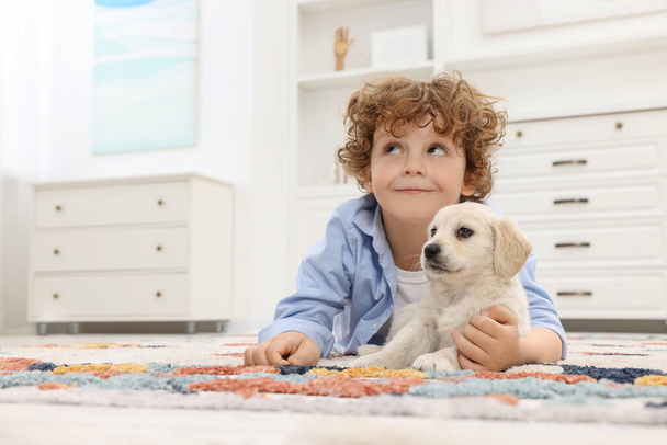 Kleine jongen liggend met schattige puppy op tapijt thuis. Ruimte voor tekst - Foto, afbeelding