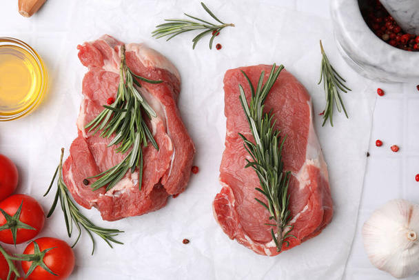 Fresh raw meat with rosemary, oil, tomatoes and spices on white tiled table, flat lay - Фото, изображение