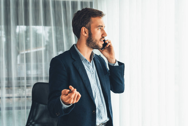 Hardworking businessman stand confidently in modern office making persuasive sales call to client. Office worker talking on the phone coordinate and manage business work with colleagues. Entity - Foto, afbeelding