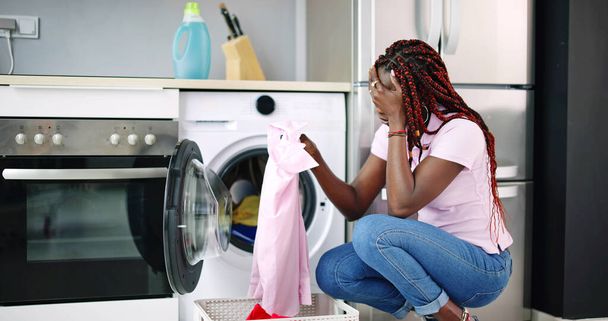 Mladá žena, krčí se vyčistit oblečení poblíž elektronická pračka - Fotografie, Obrázek