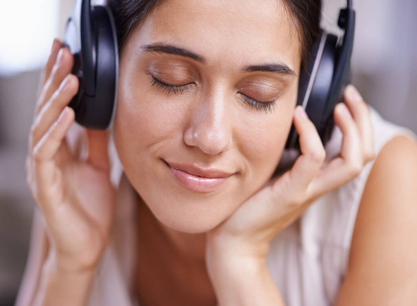 Calm woman, headphones and listening to music with smile on sofa for free time, comfort or relaxing at home. Female face smiling on living room couch with headset for audio sound track or relaxation. - 写真・画像
