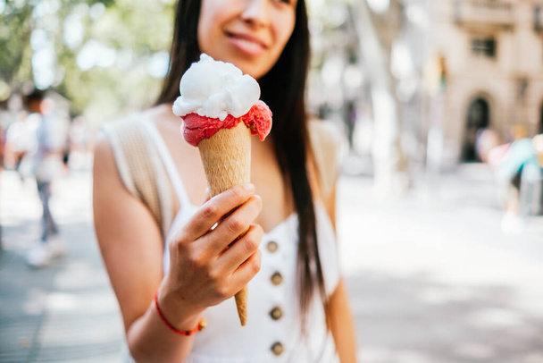 Enfoque suave de cultivo femenino hispano demostrando cono de oblea con helado en el soleado día de verano en la calle de Barcelona, España - Foto, imagen