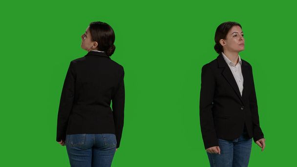 スタジオで待っている、緑の背景の上に立って訴訟で楽観的なビジネス女性のクローズアップ。スタイリッシュでカメラに自信を持って行動する社員、会社の労働者. - 写真・画像