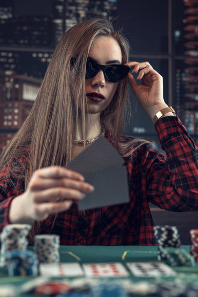 Beautiful caucasian woman looking at poker cards and doing makes a bet, raises. Winning concept - Zdjęcie, obraz