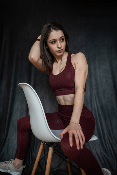 Atlética morena joven mujer usar sujetador clort sentado en la silla en sesión de estudio. Estilo de vida deportivo - Foto, Imagen