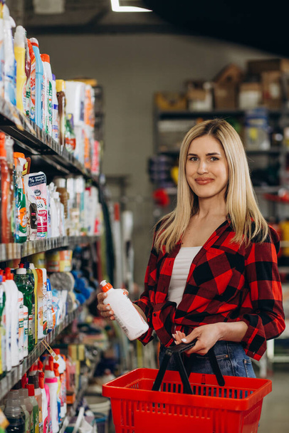 İlgi çekici genç bir kadın ev kimyasalları dükkanından bir şeyler alıyor, şişelerin üzerindeki etiketleri okuyor. - Fotoğraf, Görsel