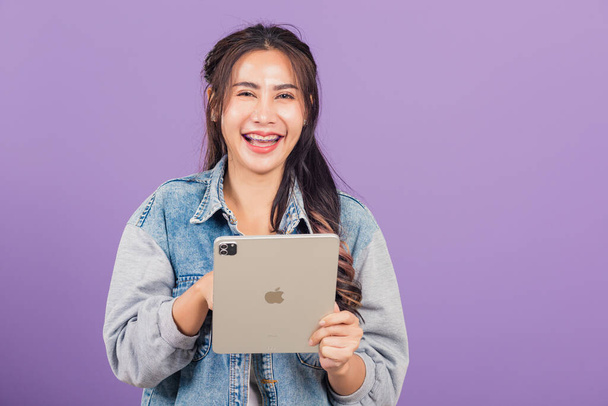 Portrait of Asian beautiful young woman smiling using tablet computer, Happy lifestyle female teen touching screen on digital tablet pc, studio shot isolated on purple background - Fotó, kép