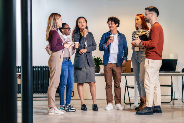 Счастливые разнообразные коллеги веселятся на обеденном перерыве в офисе, улыбаясь мультирасовые сотрудники смеются и говорят пить кофе - Фото, изображение