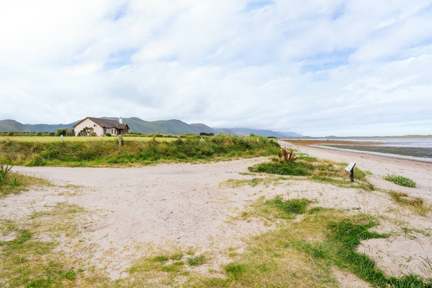 Discover tranquility in coastal Ireland as you gaze upon a picturesque house nestled amidst sandy dunes, lush greenery, and the vast expanse of the ocean. - Photo, Image