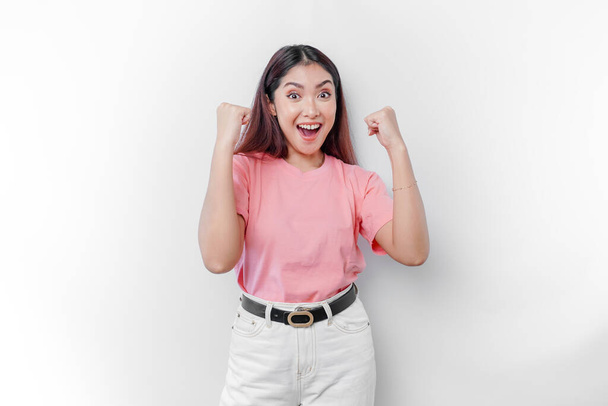 Una joven asiática con una feliz expresión exitosa usando una camiseta rosa aislada por un fondo blanco - Foto, Imagen