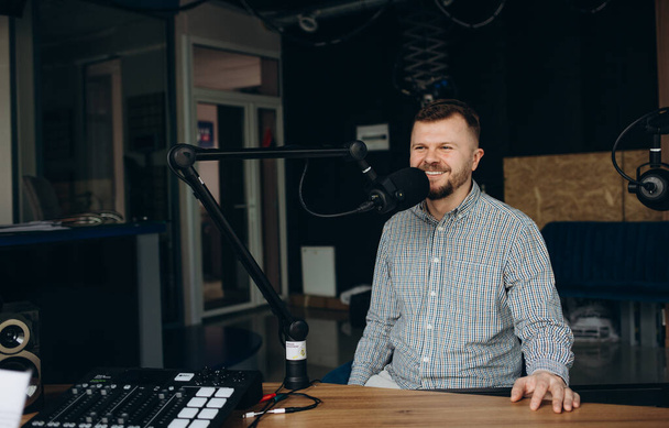 The DJ hosts the program and communicates with the audience on air at the radio station. The announcer reads the news. A male radio host speaks into a microphone and records a podcast - Valokuva, kuva