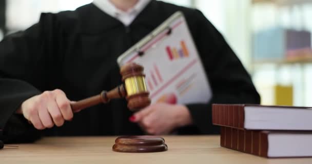女性はチャート付きの紙を保持サウンドブロック上の木製の砂利でノックします。裁判官は、審問される金融犯罪の行動を評価するための文書を審査する - 映像、動画