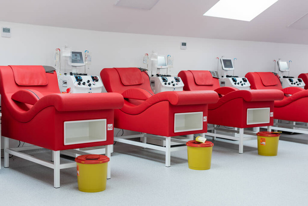 fila de sillas médicas modernas y cómodas cerca de máquinas de transfusión con pantallas táctiles, soportes de goteo con bolsas de infusión, cubos de basura en ambiente estéril de centro de donación de sangre - Foto, imagen