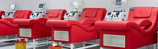 fila de cómodas sillas médicas con diseño ergonómico, cubos de basura y máquinas de transfusión automatizadas con monitores en el moderno centro de donación de sangre, pancarta - Foto, Imagen