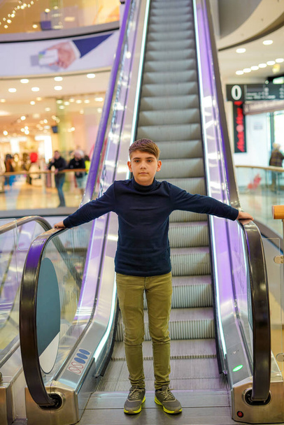 A young guy stands in front of an escalator in a shopping mall and holds on to the handrails. High quality photo - Foto, Imagen