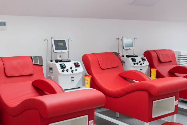 comfortabele medische stoelen met ergonomisch ontwerp in de buurt van plastic bekers en geautomatiseerde transfusiemachines met touchscreens in steriele omgeving van bloeddonatiecentrum - Foto, afbeelding