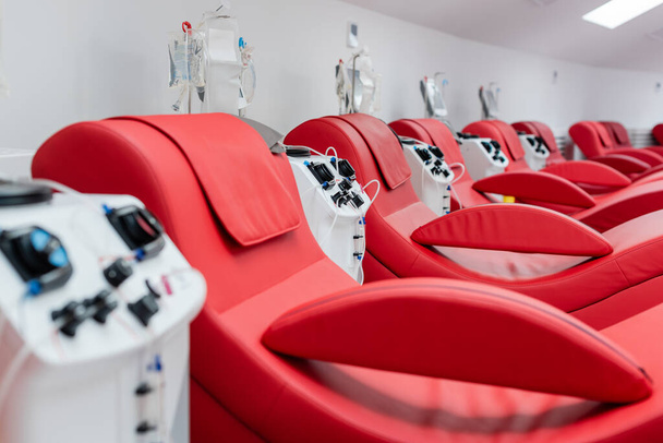 fila de cómodas y ergonómicas sillas médicas cerca de máquinas de transfusión automatizadas y soportes de goteo con bolsas de infusión en el moderno laboratorio del centro de donación de sangre - Foto, Imagen