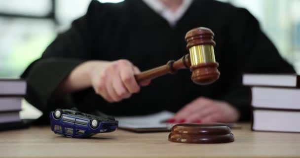 Vrouwelijke rechter in mantel klopt houten hamer zitten aan tafel met omgekeerde speelgoedauto. Ongevallen- en geschillenbeslechting in de rechtbank slow motion - Video