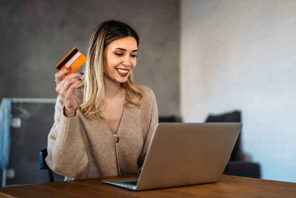 Technologie, personnes et concept d'achat en ligne. Joyeux sourire femme avec ordinateur portable et carte de crédit à la maison - Photo, image