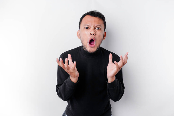 The angry and mad face of Asian man in black shirt isolated white background. - 写真・画像