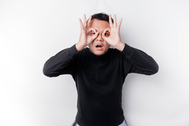 Funny obvious peeking Asian man in black shirt isolated on white background. - Photo, Image