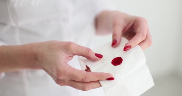 女性は軽い前提で血液染色を持つ紙組織を保持しています.女性はフラットルームで赤い斑点のナプキンを示しています。出血傷や体の傷害の結果遅い動き - 映像、動画