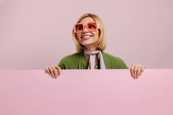 Studio shot of fashionable young woman looking out of the pink copy space and smiling - Foto, immagini