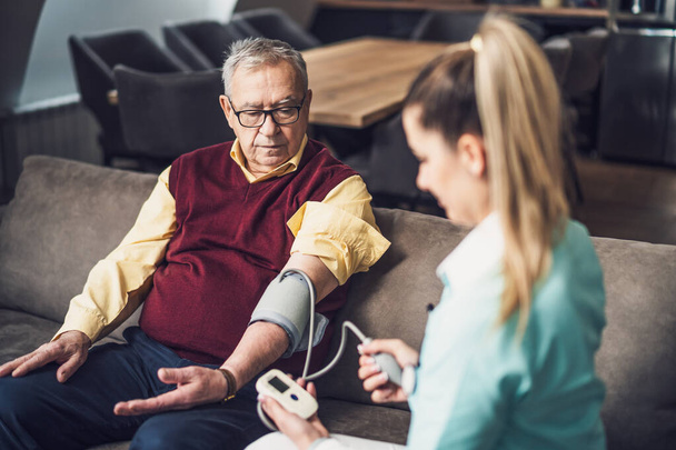 Der Hausarzt misst zu Hause den Blutdruck eines alten Mannes. Professionelle Gesundheitsunterstützung für ältere Menschen. - Foto, Bild