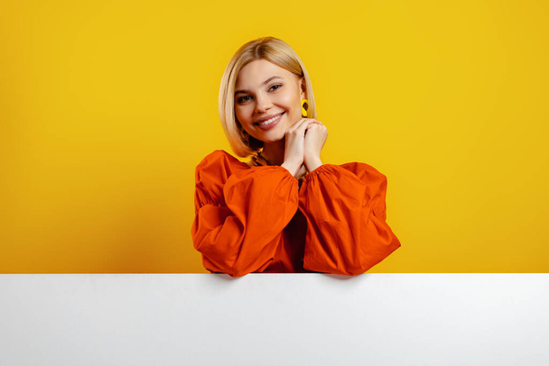Attractive young woman leaning on copy space and smiling against yellow background - Fotografie, Obrázek