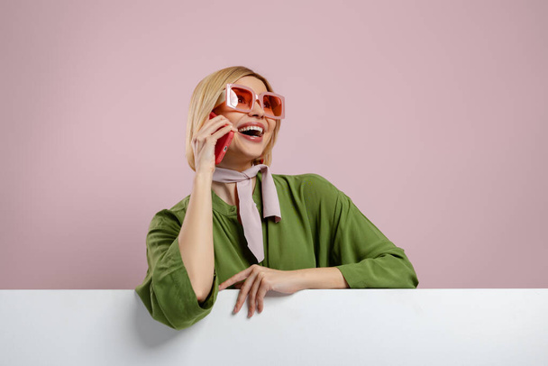 Fashionable young woman talking on mobile phone and smiling against pink background - Foto, immagini