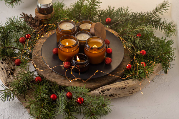 Soy candles burn in glass jars. Comfort at home. Candle in a brown jar. Scent and light. Scented handmade candle. Aroma therapy. Christmas tree and winter mood. Cozy decor. Festive garland decoration - Foto, immagini