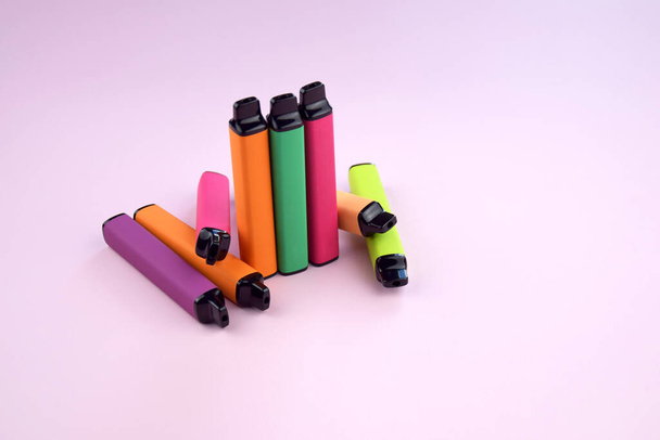 Set of multicolor disposable electronic cigarettes on a pink background. The concept of modern smoking, vaping and nicotine. - Fotografie, Obrázek