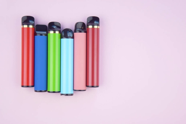 Набір різнокольорових одноразових електронних сигарет на рожевому тлі. Концепція сучасного куріння, паріння та нікотину
. - Фото, зображення