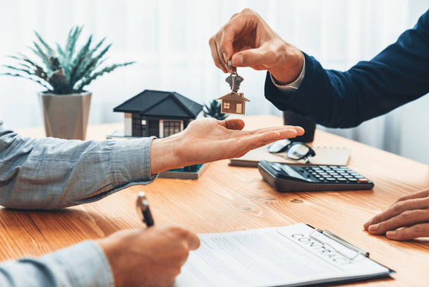 Real estate agent handing house key to buyer after signing rental least contract during house loan meeting. Successful property sale purchase agreement for new home ownership. Entity - Photo, Image