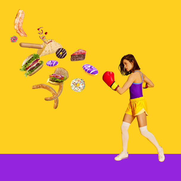 Healthy, slim, sportive woman fighting with junk, unhealthy food over bright yellow background. Burgers, sweets. Contemporary art. Food, creativity, sportive, healthy lifstyle concept. Modern design - Fotó, kép